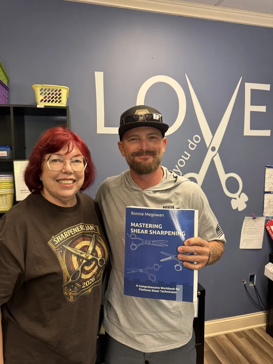 Justin Pratt standing with Bonnie Megowan, who smiles beside him as he holds her book Mastering Shear Sharpening